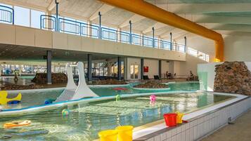 Una amplia piscina interior con diseño moderno, que incluye un elemento de onda blanca y una pared de piedra.