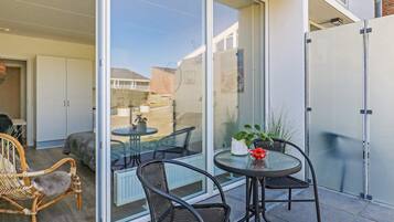 A modern outdoor patio with a glass door leading to a room, two black wicker chairs, a small round table with a bowl of fruit, and a potted plant.