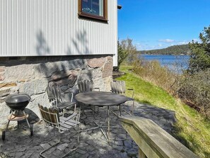 A stone patio with outdoor furniture, a grill, and a view of a lake.
