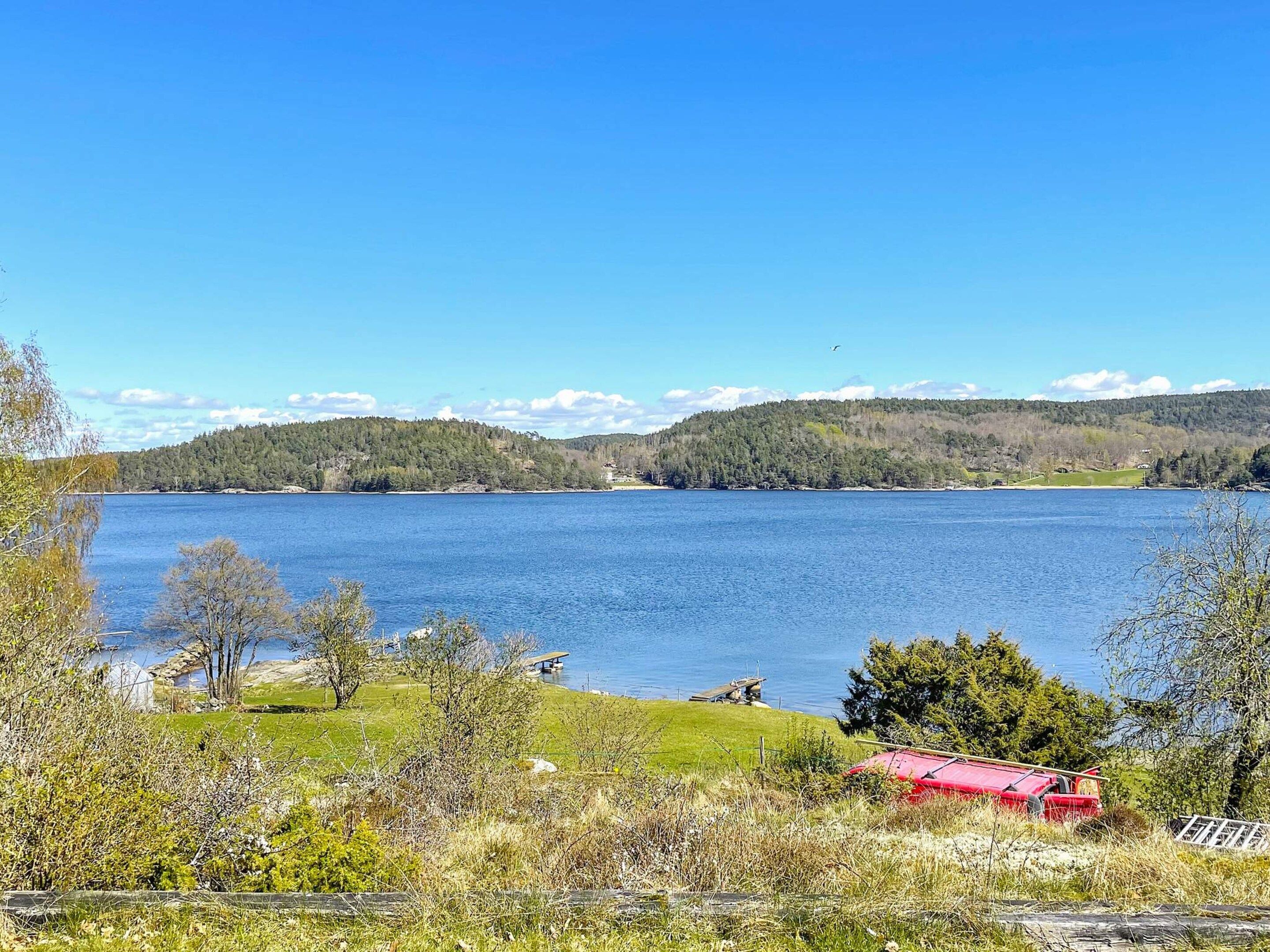 A lake with a red boat on the shore, surrounded by trees and hills.