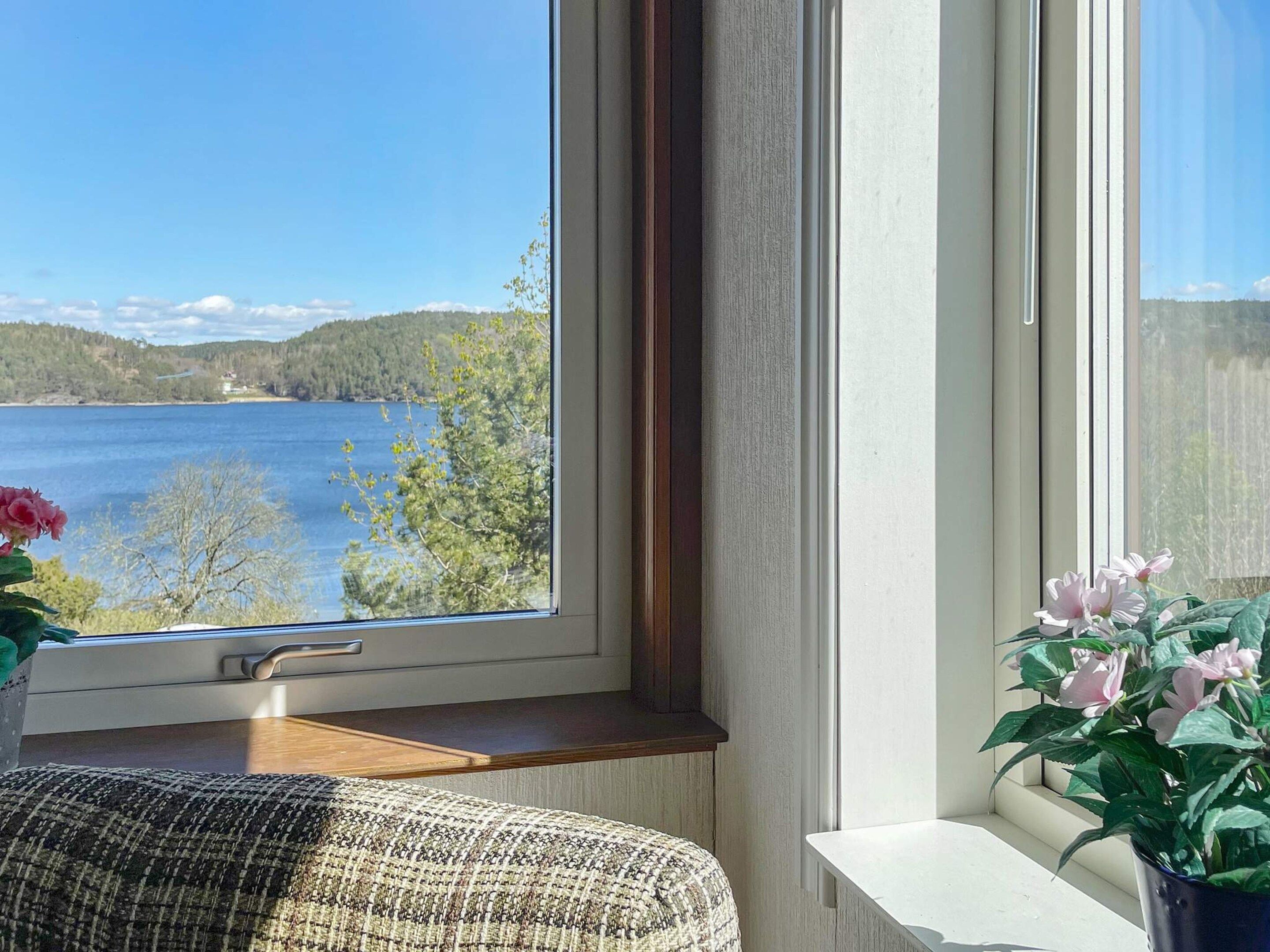 A room with a view of a lake and hills, a window sill with a plant, and a piece of furniture.