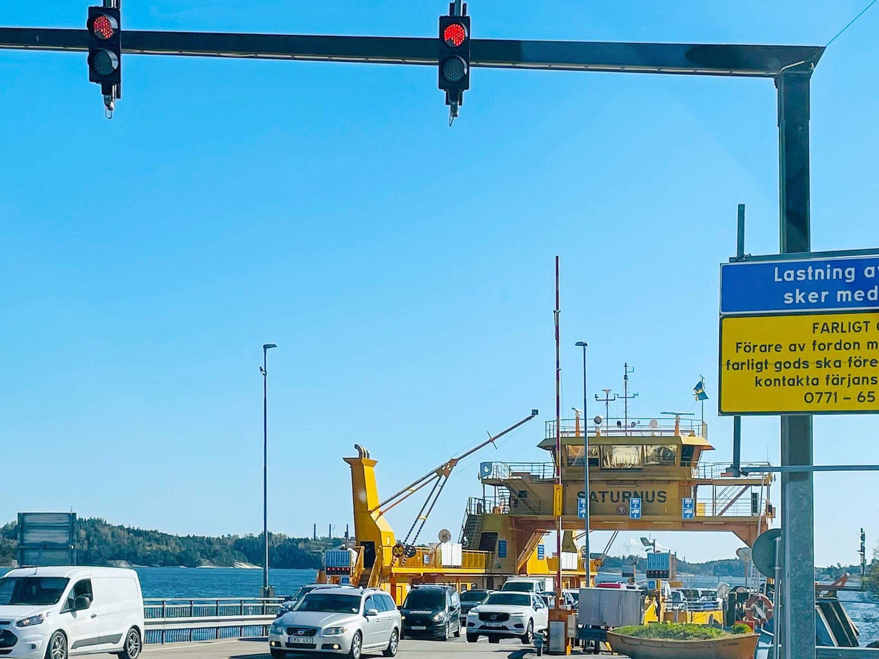 A ferry terminal with a yellow control tower, vehicles, and a clear blue sky.