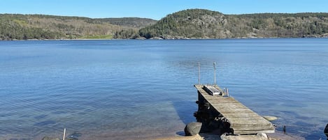 A wooden pier extending into a calm lake with a forested hill in the background.