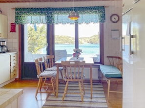 A dining area with a table and chairs, a view of the sea, and a clock on the wall. - 5 Person Holiday Home in Stillingson (Stillingsön)