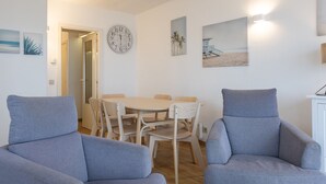 Een moderne woonkamer met een ronde tafel en twee grijze fauteuils, een wandklok en decoratie met een strandthema.