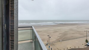 Uitzicht op het strand vanaf een balkon, met een bakstenen muur en een glazen hekwerk.