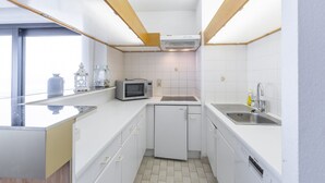 Een compacte keuken met witte kasten, een ingebouwde magnetron, een vaatwasser en een spoelbak.