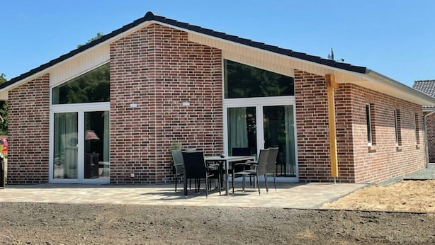 Een modern gebouw van baksteen met grote ramen en een patio met terrasmeubilair.