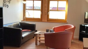 Een woonkamer met een zwarte leren bank, een rode fauteuil, een kleine tafel en een tv-meubel.