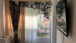 A bedroom with a bed, a window with curtains, a TV mounted on the wall, and a small bedside table. - Belvilla by OYO Apartamento Divendres (Massanassa)