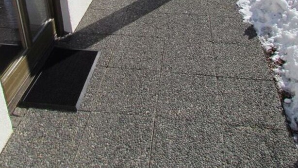 Une allée extérieure couverte qui mène à un bâtiment doté d’une porte et de fenêtres en verre.