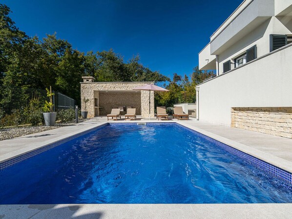 Une piscine avec des chaises longues, une structure en pierre et un bâtiment moderne.