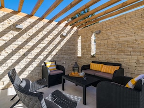 A covered patio area with stone walls, wooden beams, wicker furniture, and a table with a tray of items. - Villa Adrimar Comfortable Holiday Residence (Vrbnik)