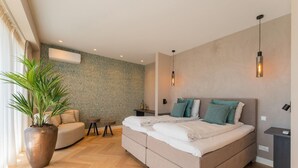 Een moderne slaapkamer met een groot bed, een kamerplant, een klein tafeltje en een bank.