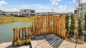 Een houten omheining die leidt naar een waterpartij, met een modern gebouw op de achtergrond.