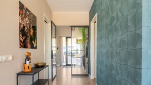 Een hal met een modern design, met een houten vloer, een zwarte console tafel met een fles en een schaal, en een groot kunstwerk in een lijst aan de muur.