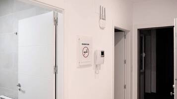 Baño con pared de azulejos blancos, secamanos y un cartel que prohíbe fumar.