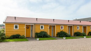 Un bâtiment jaune avec un toit recouvert de tuiles rouges, une allée pavée et de petits arbustes devant.