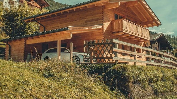 A wooden chalet with a balcony, surrounded by lush greenery and a car parked in front. - Saerbecker Berghutte (Heiligenblut)