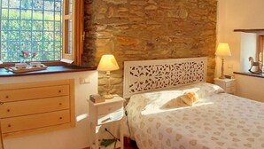 Une chambre avec un mur en pierre, une commode en bois, un lit recouvert d’une couvre-lit à motifs et deux lampes de chevet.