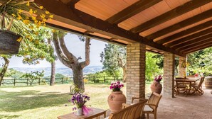 Un patio al aire libre con muebles de madera, macetas de terracota con flores y vistas al campo.