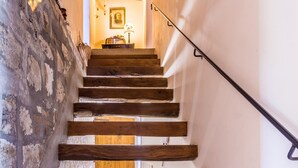 Una escalera de madera con barandilla que conduce a una habitación con una lámpara y un cuadro en la pared.