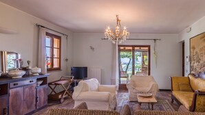 Una sala de estar con televisor, candelabro y vista a un espacio exterior a través de un ventanal.