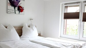 A bedroom with a bed, pillows, a nightstand, a wall clock, and a window with blinds. - Pear - On the Fruit Tree (Golssen)