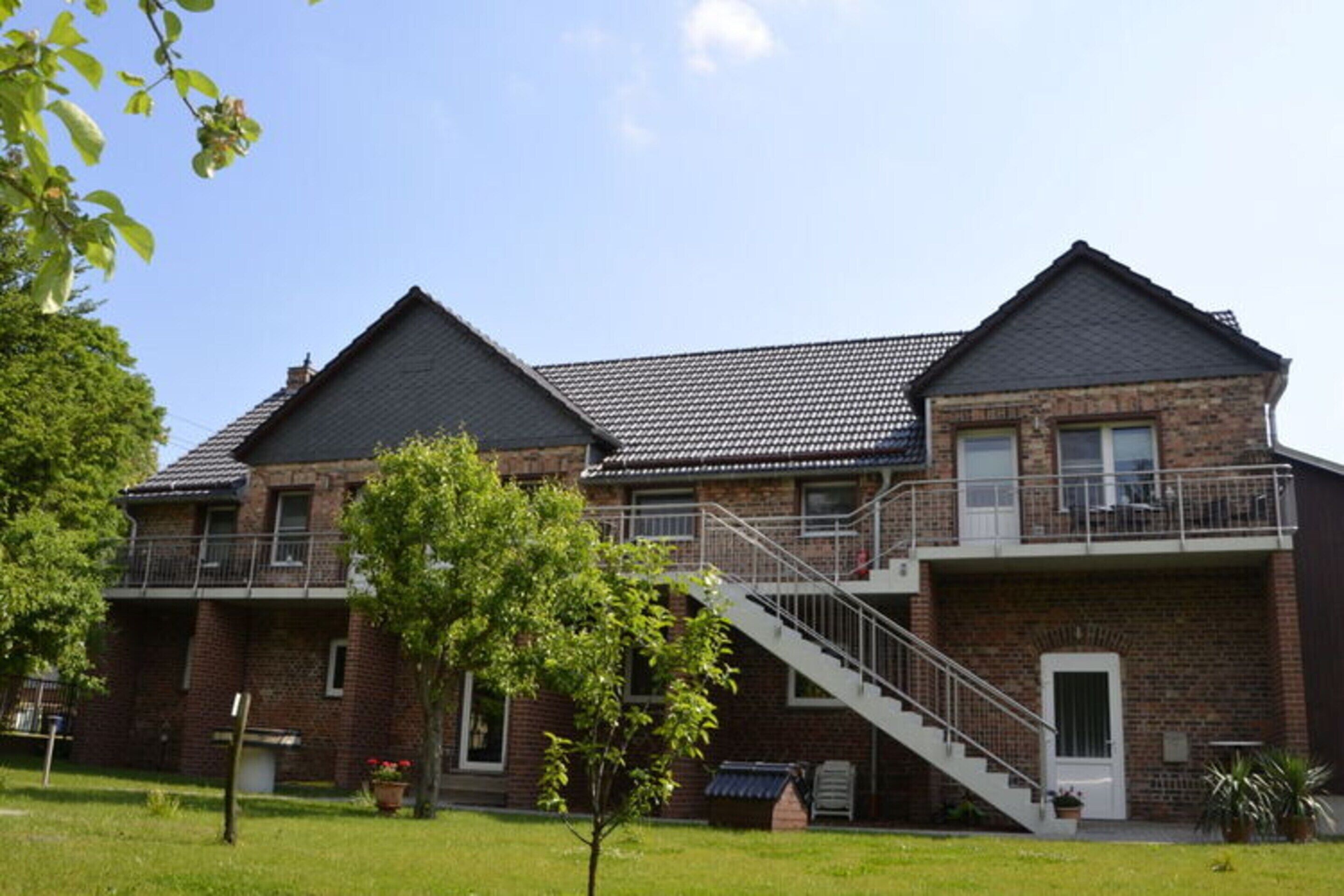 Un bâtiment à deux étages, construit en briques, avec un balcon au niveau supérieur et un escalier menant à l’entrée.