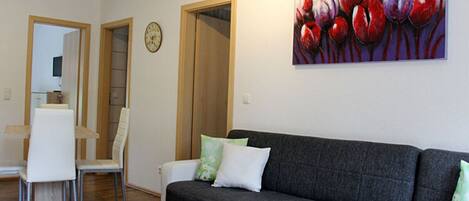 A living room with a grey sofa, white chairs, a wooden coffee table with a book, and a painting of flowers on the wall.