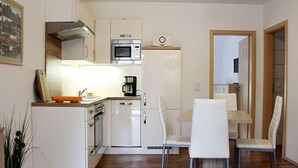 A compact kitchen with white cabinetry, a microwave, and a coffee maker. There are white chairs around a small dining table. - Pear - On the Fruit Tree (Golssen)