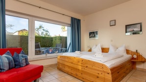Une chambre à coucher avec un lit en bois, un canapé rouge et une grande fenêtre avec des rideaux.
