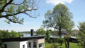 Une maison moderne avec un toit plat, une cheminée et un petit jardin comprenant une pelouse et quelques arbres.