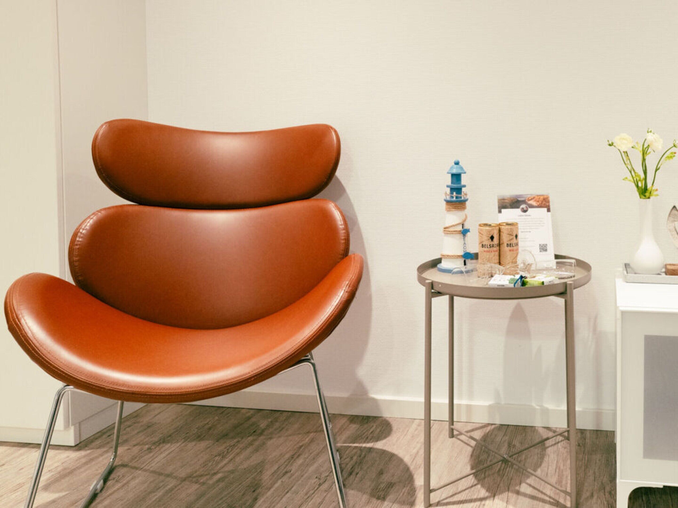 A brown leather chair with a metal frame, a small round table with a tray holding a bottle, boxes, and a vase with flowers.