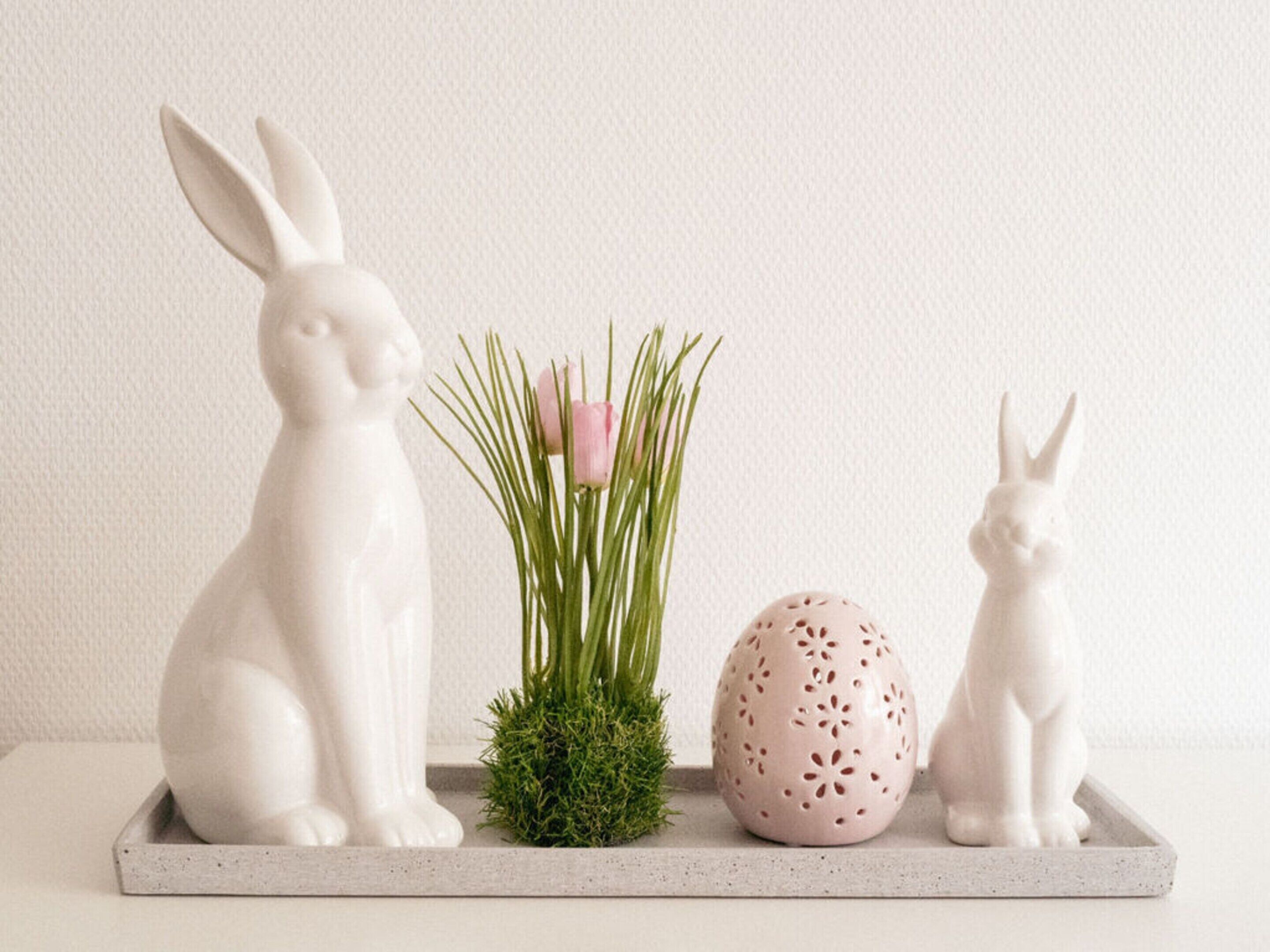 Une figurine de lapin en céramique blanche, un œuf de Pâques rose et une plante verte, le tout posé sur une étagère blanche.