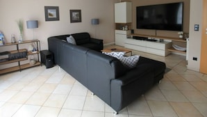 Un salon moderne avec un canapé noir, un téléviseur à écran plat et un design minimaliste.