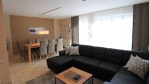 Un salon moderne avec un canapé d’angle, une table basse en bois et un coin repas comprenant une table et des chaises.