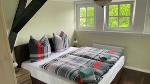 Une chambre à coucher avec un lit, deux fenêtres, un radiateur et une table de chevet.