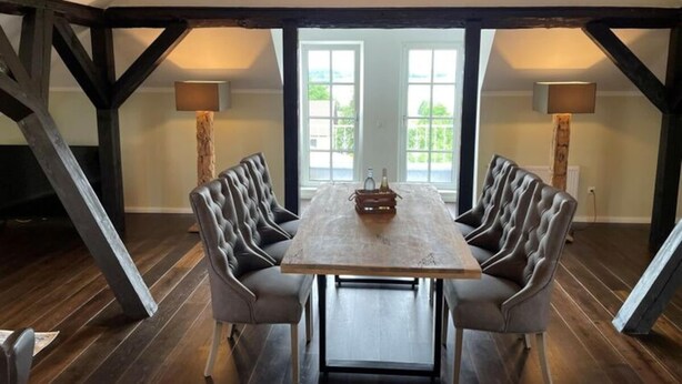 Un espace repas avec une table en bois et des chaises en cuir, situé sous un plafond voûté aux poutres apparentes.