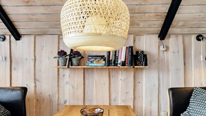 Une table à manger en bois, surmontée d’un luminaire tressé, entourée d’étagères et de deux canapés en cuir.