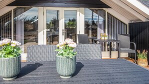 Un espace extérieur abrité, aménagé avec deux plantes en pot, une table et des chaises.