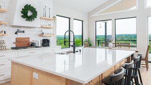 Een moderne keuken met een groot kookeiland, witte kastjes en uitzicht op het landschap door grote ramen.
