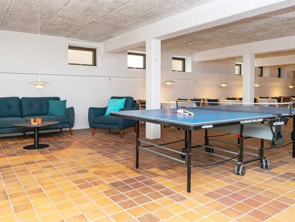 A ping pong table in a communal area with a tiled floor, sofas, and tables.
