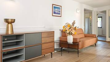 Una sala de estar moderna con un sofá, una mesa de centro de vidrio, un aparador y un jarrón con flores.