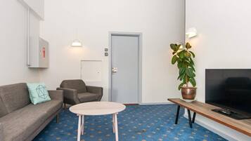 Una sala moderna con un sofá, una mesa redonda para café, un televisor sobre un mueble, una planta en maceta y una puerta con el símbolo del número.