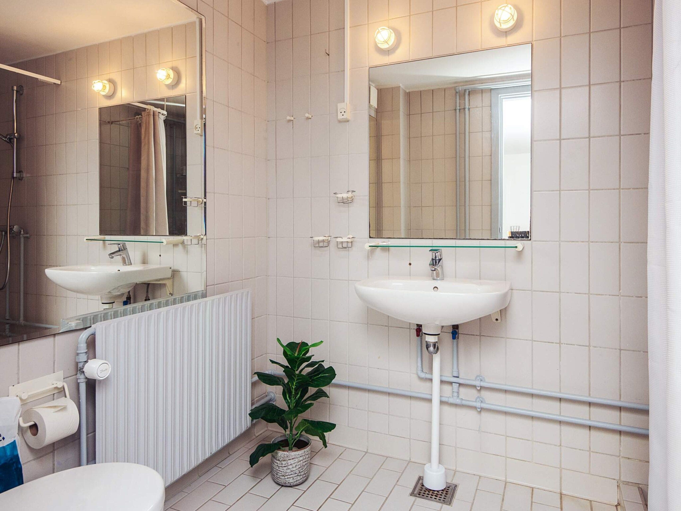 Un baño con lavabo blanco, espejo, ducha y planta en maceta.