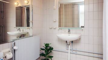 Un baño con lavabo blanco, espejo, ducha y planta en maceta.