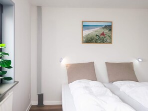 A bedroom with a bed, a wall-mounted picture, and a plant on a shelf.