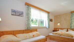 Een kamer met twee houten bedden, een raam met gordijnen, een schilderij aan de muur en een nachtkastje met een lamp.