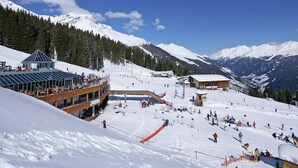 Een wintersportgebied met een glazen gebouw, skipistes en met sneeuw bedekte bergen.